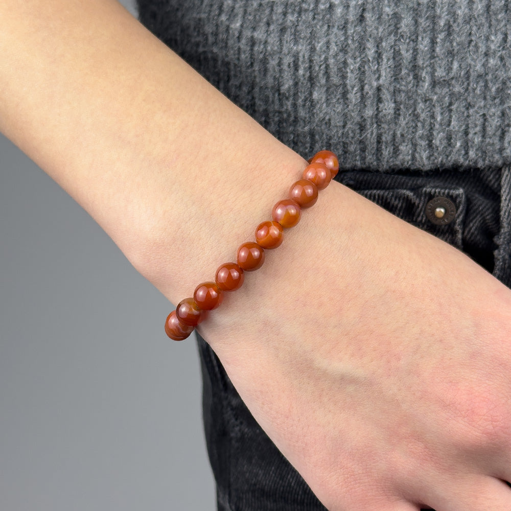 Person wearing a red beaded bracelet on a neutral background