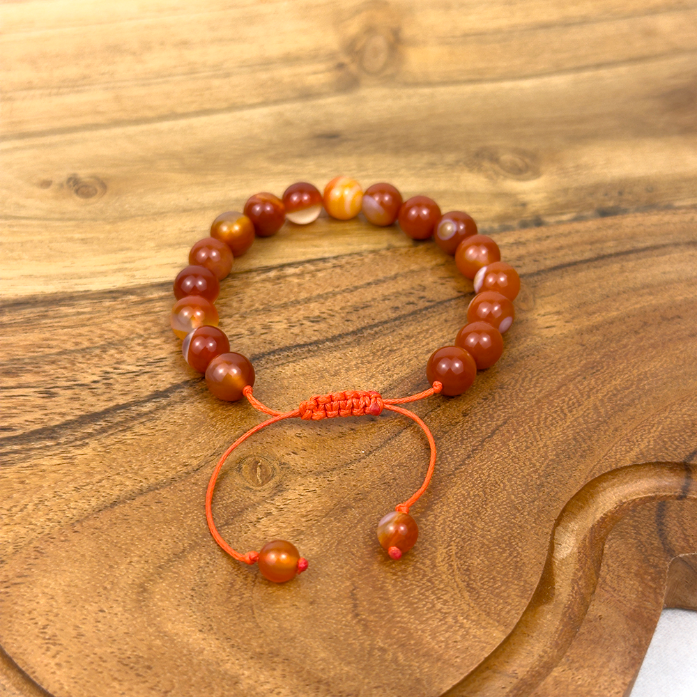 Beaded bracelet with orange cord on a wooden surface