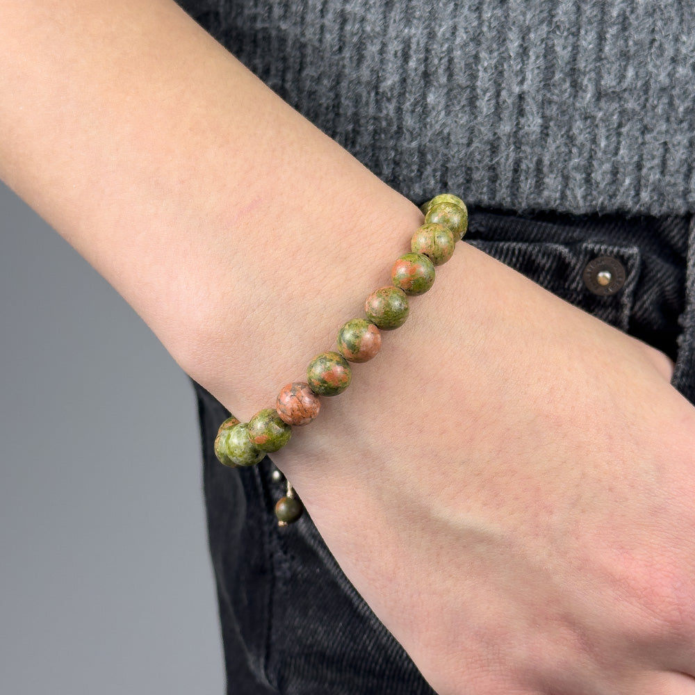 Bracelet with green and pink beads on a wrist against a gray background