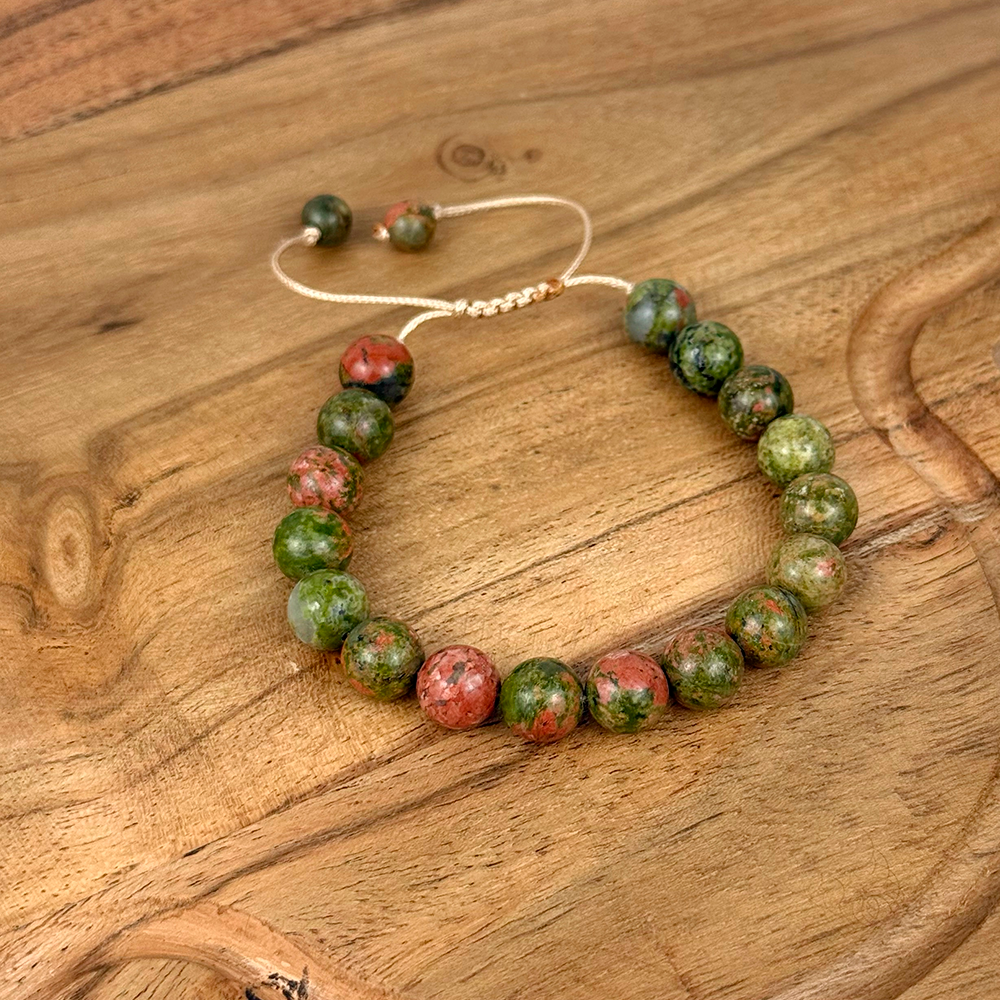Beaded bracelet with green and red stones on a wooden surface