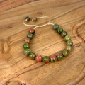 Beaded bracelet with green and red stones on a wooden surface